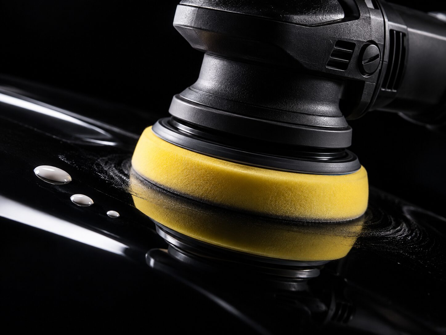 Polisher with a yellow pad on black paint